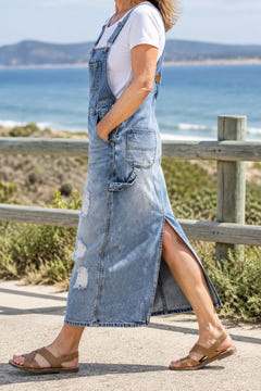 Back-slit denim overall dress in light blue on a coastal walk